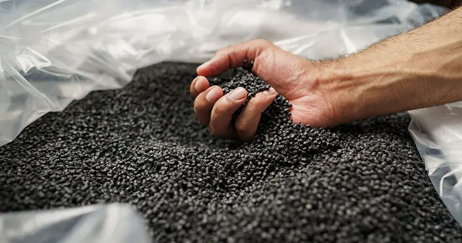 a person's hand scooping up black, plastic pellets